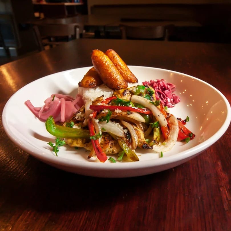 Cuban chicken fajitas with peppers, onions, rice, plantains, and pickled red onions on a white plate.