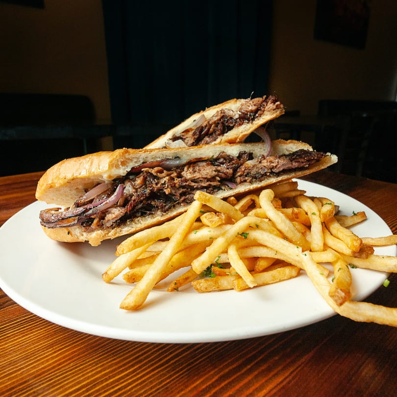 A steak and onion sandwich on a white plate with a side of golden french fries.