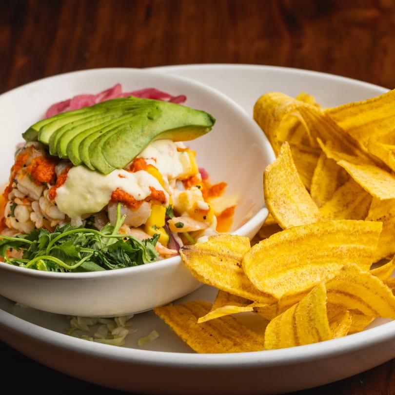 Ceviche with avocado, red sauce, and green herbs, served with a side of plantain chips.